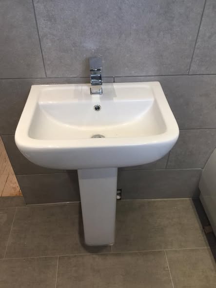 White pedestal basin and chrome tap against grey bathroom tiles